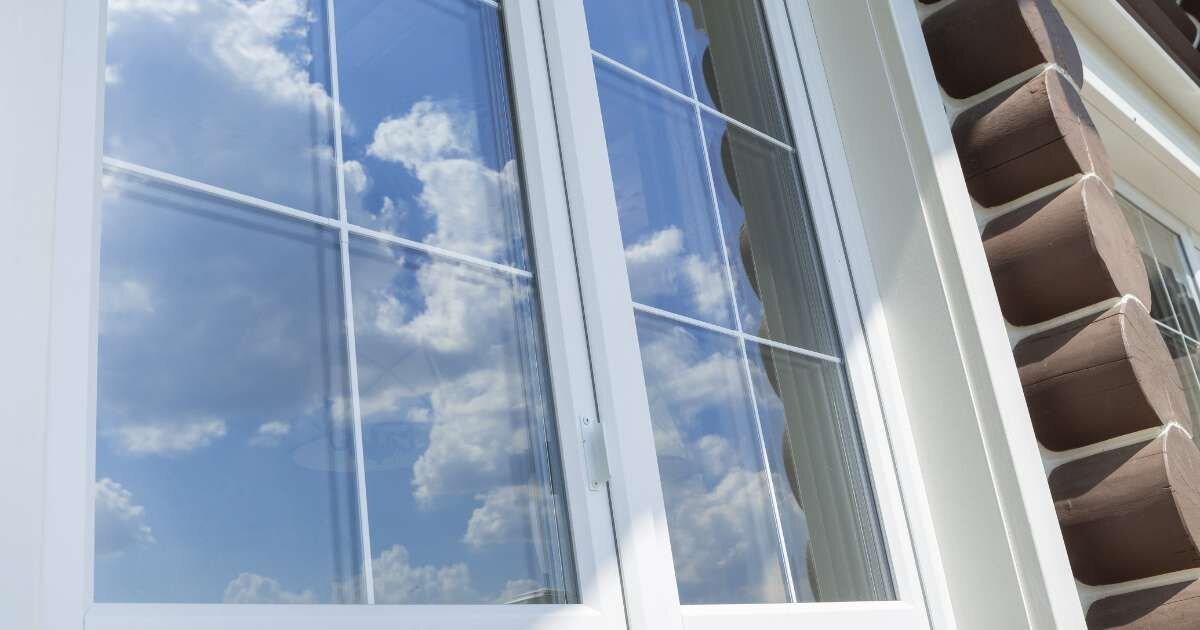 Window reflection: White-framed window reflecting a blue sky with clouds.